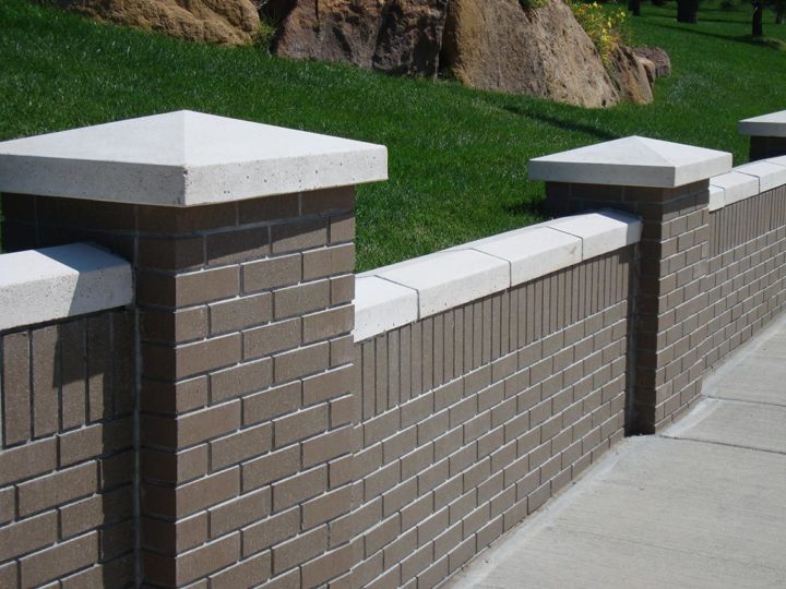 closeup of a brown-colored thin brick wall with gray accents and concrete sidewalk in front of a grassy hill