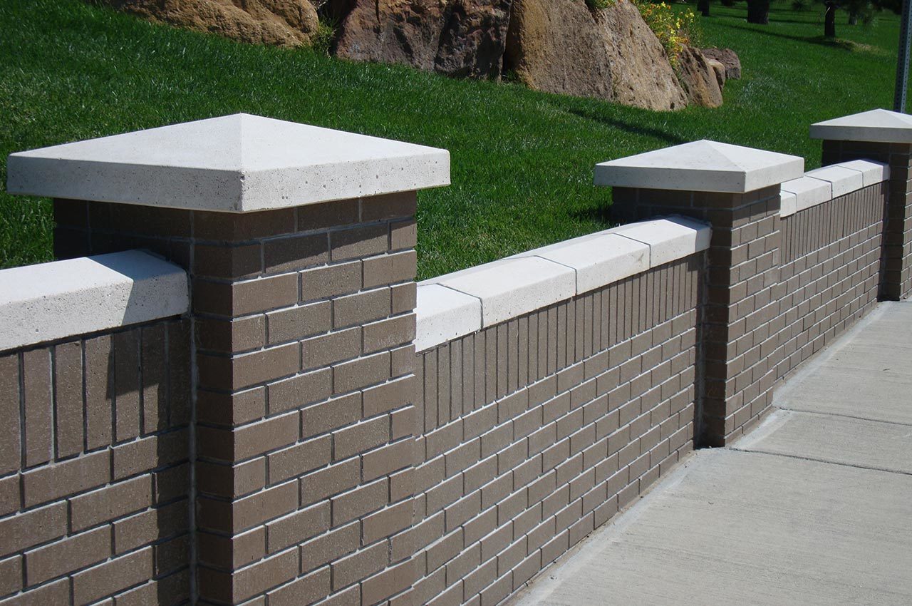 closeup of a brown-colored thin brick wall with gray accents and concrete sidewalk in front of a grassy hill